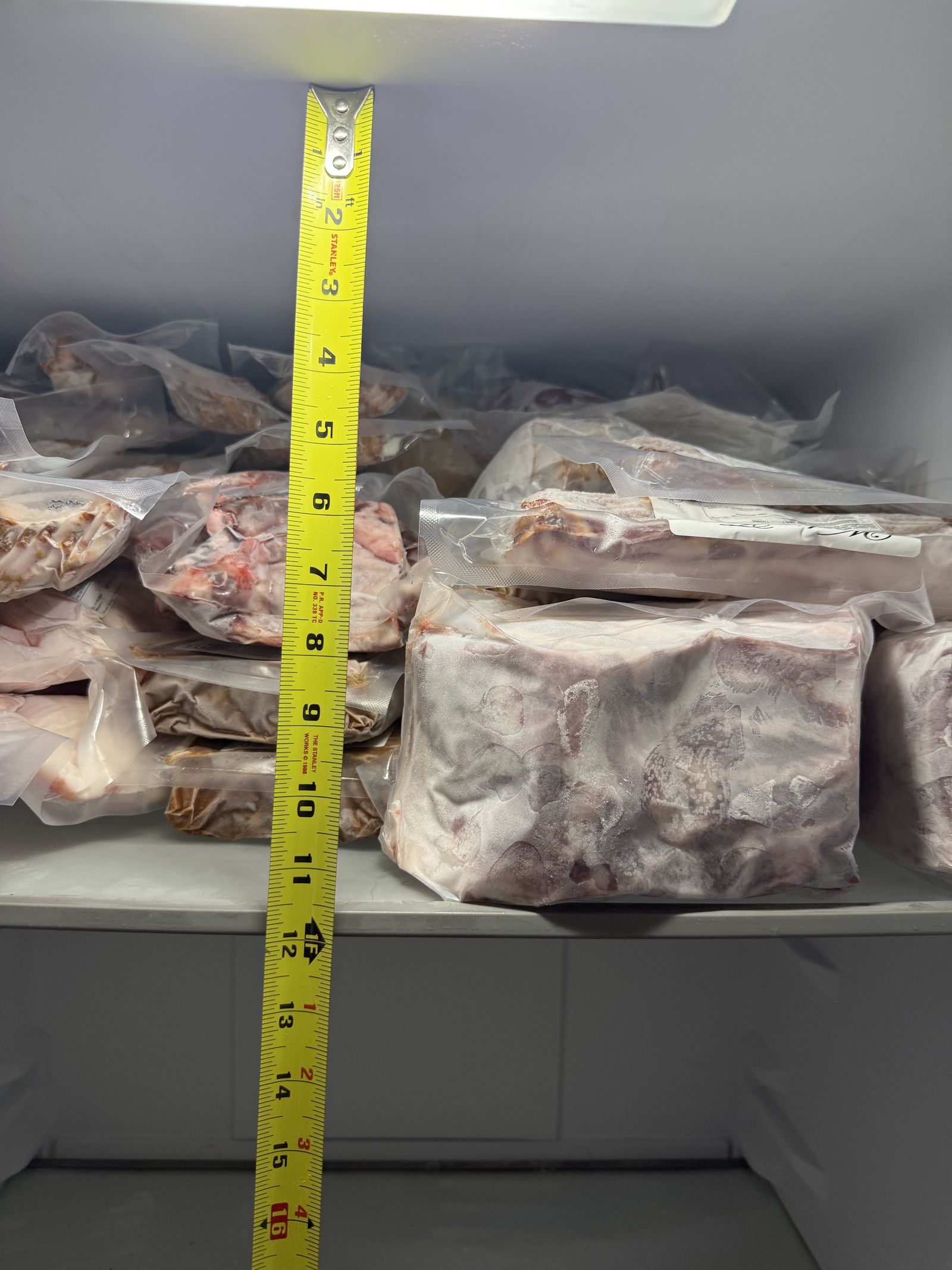 Close-up of vacuum-sealed pork cuts in the freezer, with a tape measure showing approximate package sizes