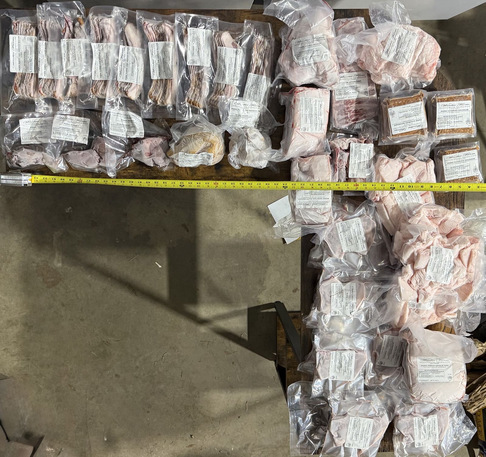 A complete half-hog share laid out - roasts, chops, ground pork, and specialty cuts arranged with a tape measure for scale